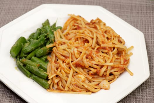 Homemade cooked meal of green steamed asparagus with butter and linguine with garlic cloves and tomato sauce. Linguini pasta with tomato sauce and garlic cloves and green asparagus with butter meal.