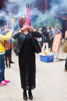 Chinese woman in prayer with incense sticks