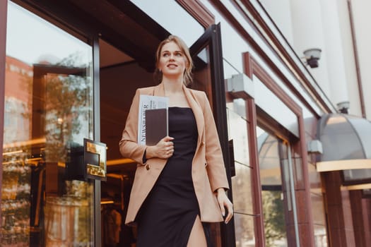 Young well dressed smiling business woman with tablet pc leaving building, summer day outdoors