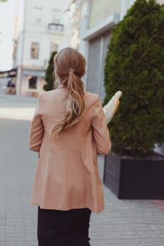 Business woman in a rush, carrying baguettes and takeaway hot beverage. Street portrait, back view.