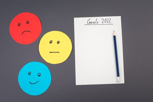 Empty paper with goals 2022, copy space for text, pen, blue colored background, business concept, making plans for the new year, happy and sad faces