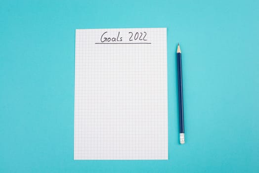 Empty paper with goals 2022, copy space for text, pen, blue colored background, business concept, making plans for the new year
