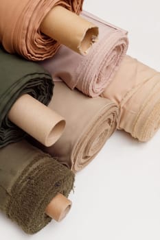 Stack of pastel color fabric rolls of synthetic and natural fabrics.