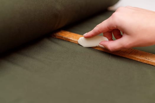tailor marks up textile using soap and wooden ruler on pattern cutting.