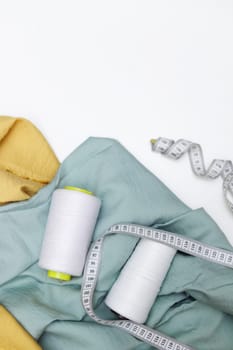Various fabrics, measuring tape and thread isolated on white. Flat lay