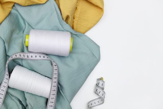 Various fabrics, measuring tape and thread isolated on white. Flat lay