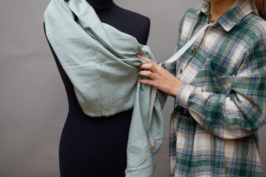 Young woman fashion designer measuring mannequin, seamstress holding tape working with dummy in cozy home or tailor shop, dressmaking and sewing concept, exclusive unique clothes creation