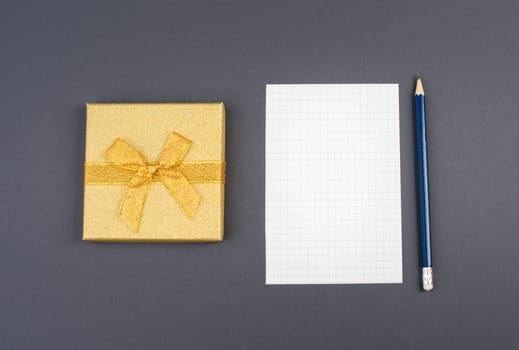 Empty paper, a pen and a golden colored gift on a dark grey background, copy space for text