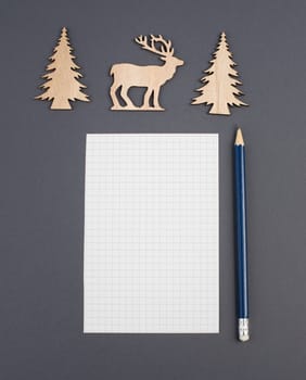 Empty piece of paper with a pen, christmas season, reindeer and wooden trees, wishing list for Santa Claus