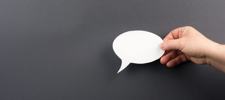 Empty speech bubble, white paper on a dark grey background, copy space for text, communication symbol