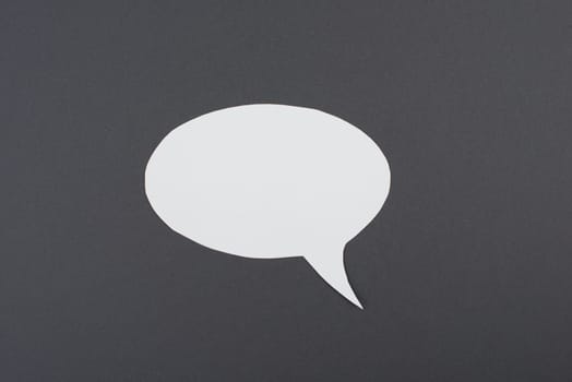 Empty speech bubble, white paper on a dark grey background, copy space for text, communication symbol