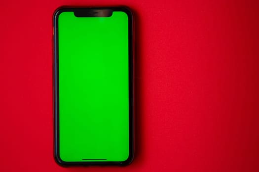 A phone with a green screen is on a red background. High quality photo