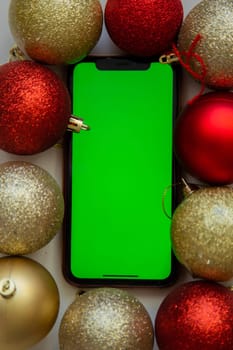 A phone with a green screen lies among the golden and red Christmas balls. High quality photo