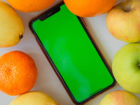 A phone with a green screen is lying among the fruits. High quality photo