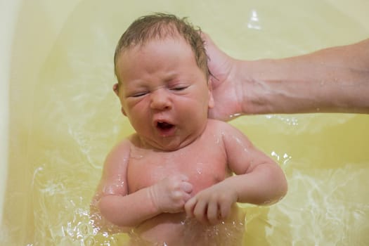 A newborn baby is bathing in a bath for the first time, his hand is holding his head, the baby is scared. High quality photo