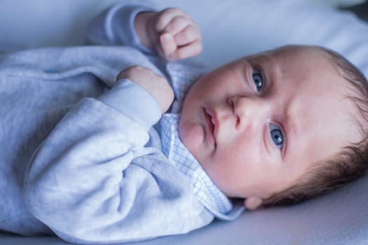 A small newborn baby with blue eyes clenching his fists and taking a boxing pose lies in a gray suit with a checkered collar on a white background. High quality photo
