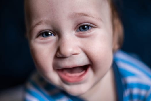 A smiling toothless kid in a striped blouse laughs, face close-up. . High quality photo