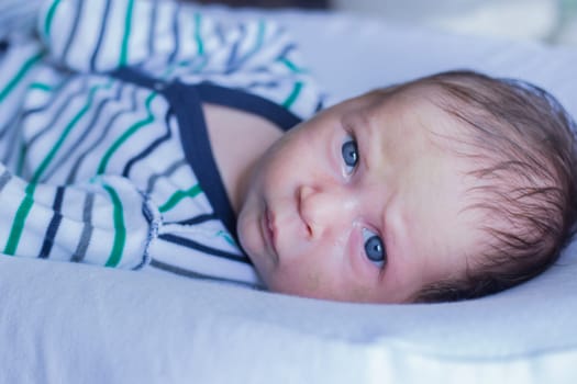A little boy in a striped suit seriously and frowns looks into the camera, lying on a white pillow. High quality photo