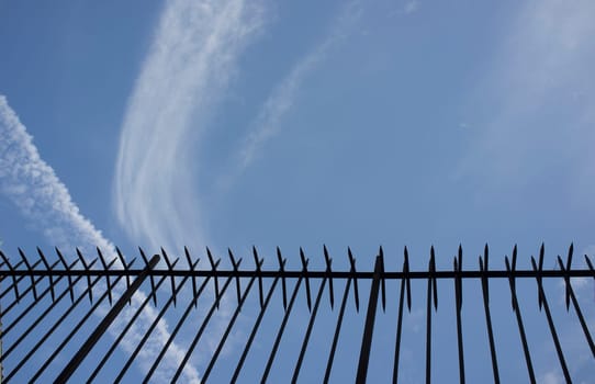 Wrought iron spiky fence placed on the top of a wall. Blue cloudy sky