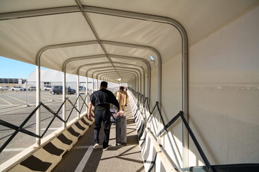 Civitavecchia, Italy - December 19, 2024: People navigating a modern pedestrian corridor at a harbor facility on a sunny day. Concept: journey, public space, urban design. (