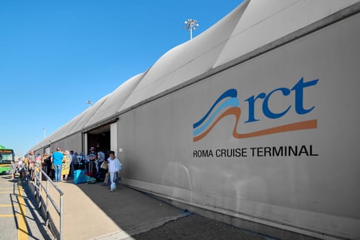 Civitavecchia, Italia - December 19, 2024: People with suitcases at Roma Cruise Terminal on a sunny day, showcasing efficient passenger services and transportation, including a green bus.