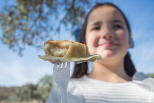 Child girl with jiaozi piece on fork. Outdoors background