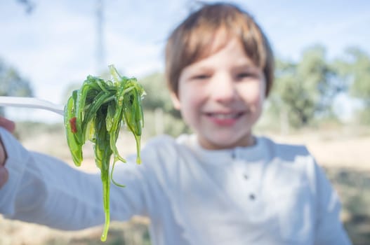 Child boy with wakame salad on fork. Outdoors background