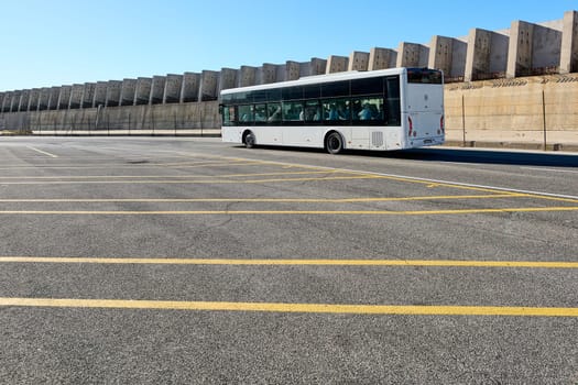 Civitavecchia, Italia - December 19, 2024: A public bus moves through the city on a sunny day, emphasizing urban mobility, infrastructure, and industrial aesthetics with a concrete barrier.