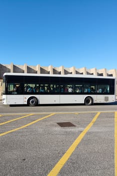 Civitavecchia, Italy - December 19, 2024: A city bus travels along a deserted street, emphasizing public transport in an urban setting The clear sky and concrete barrier offer a modern, clean backdrop