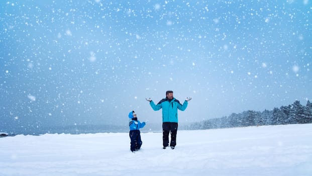 Father and his son standing on the snowfall in the snowy winter forest. Concept of the family relationship and vacation.