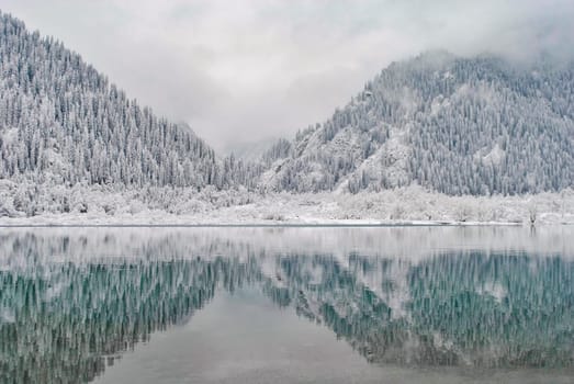 Mountain lake in winter. Snow-covered mountains are reflected in the water. Winter landscape.