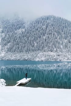 A man stands on the boat pier of a mountain lake in winter. Winter landscape.