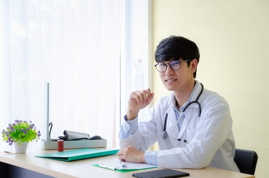 Portrait of male doctor in eyeglasses sitting at desk. Smiling young doctor waiting for a patient in hospital office. Healthcare concept.