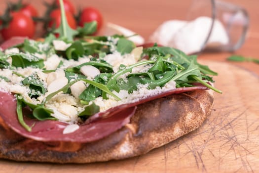 Close-up of a pizza with raw ham, parmesan cheese, almonds and rocket.