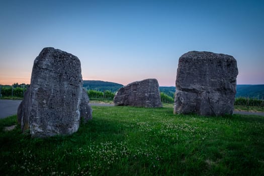 Three stone rocks on green meadow in dawn twilight