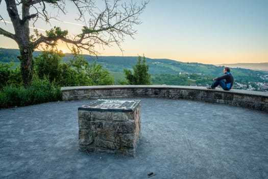 Man is sitting on a stone wall and looking at sunrise