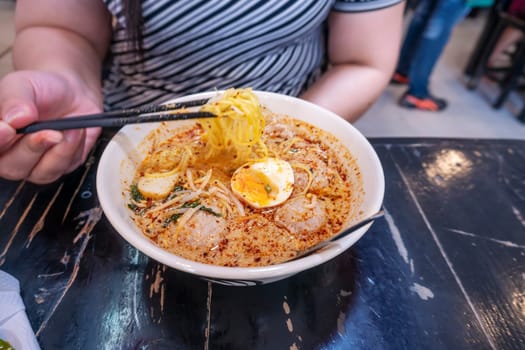women eating pork noodle tom yum with egg on blurred wooden table