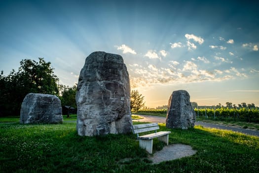Three rocks on green meadow with sunbeams in the sky with clouds.