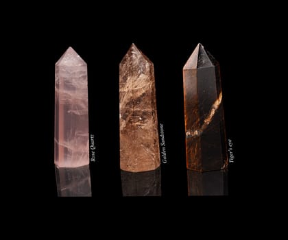 Set of crystals of semi-precious stones: rose quartz, tiger eye, golden sandstone with natural reflection isolated on black glossy background