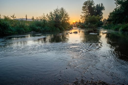 Sunrise with sunstar over river stream rems landscape