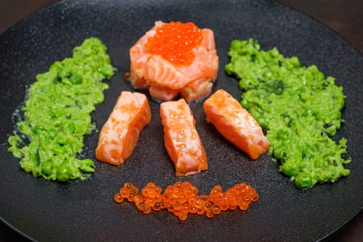 Salmon with orange caviaa an mashed peas on black plate