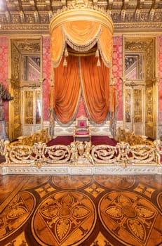 Turin, Italy - Circa August 2021: old throne room interior with chair in luxury palace. Red and gold antique Baroque style - Savoia Royal Palace