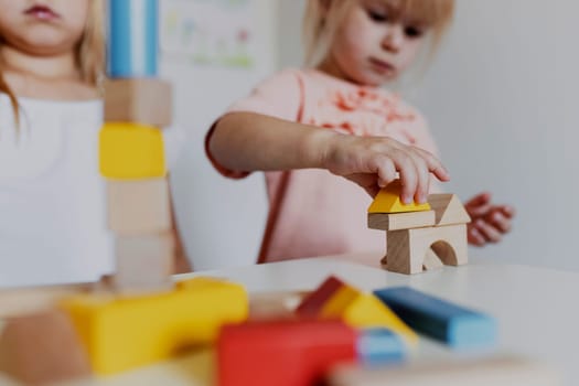 Two child girl sisters playing with colorful wooden toy building blocks. Little kid building tower or house at home or day care. Educational toy for young children. Construction block for baby toddler