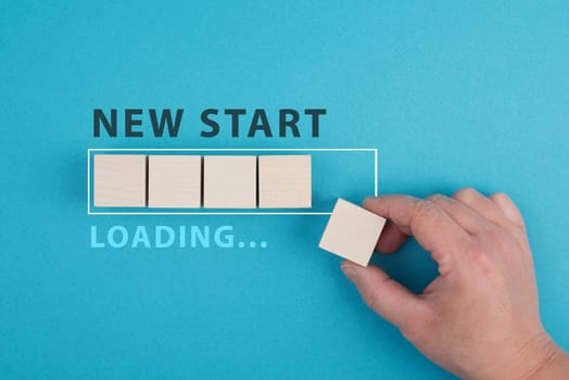 Words new start with a loading bar, hand puts last wooden cube on the blue background, message