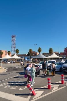 Civitavecchia. Italia  - December 19, 2024: People with suitcases walking towards the entrance of Civitavecchia port terminal. The image shows a clear blue sky, palm trees, and a busy travel scene.