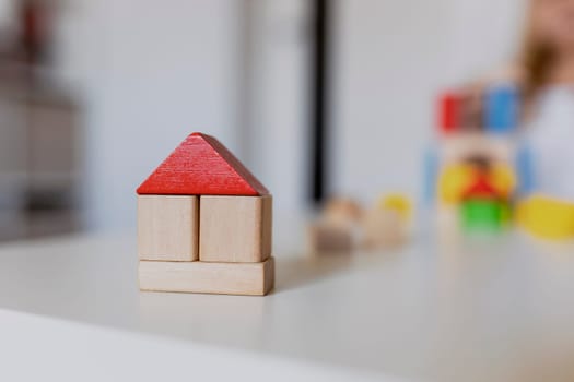 Child girl playing with colorful wooden toy building blocks. Little kid building tower or house at home or day care. Construction block for baby or toddler. Mess in kindergarten play room.