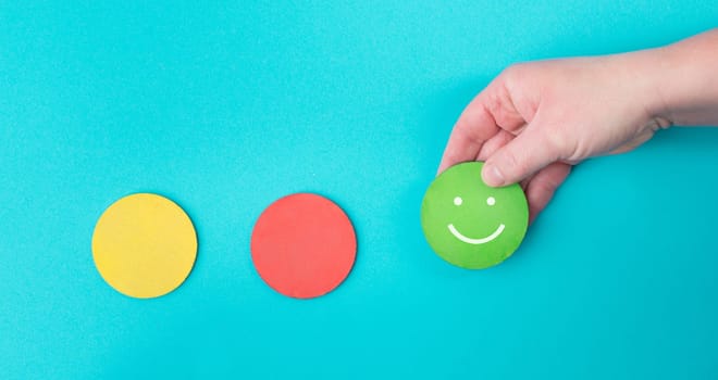 Hand holds a green smiling face, red and yellow circle empty, blue colored background, copy space, customer review