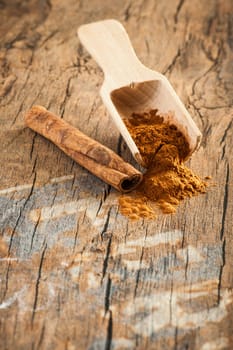 Close-up wooden scoop with cinnamon powder on an old wooden surface in an elevated view at aperture 16.