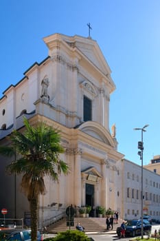 Civitavecchia. Italia - December 19, 2024: Urban street view Civitavecchia, Italy, showcasing a historic church and modern buildings under a bright blue sky Concept: City life, architectural contrast
