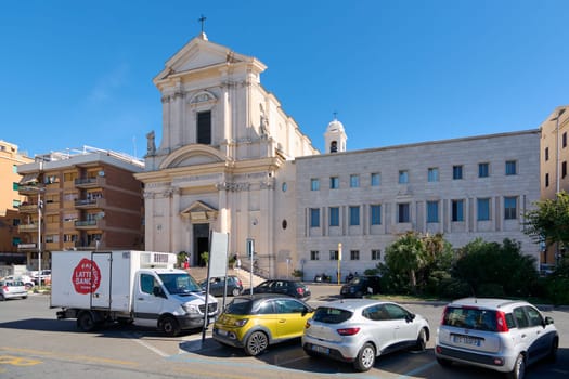 Civitavecchia. Italia - December 19, 2024: Sunlit church entrance in Civitavecchia, Italy, with surrounding modern buildings and street activity. Concept: Urban life, architectural heritage.